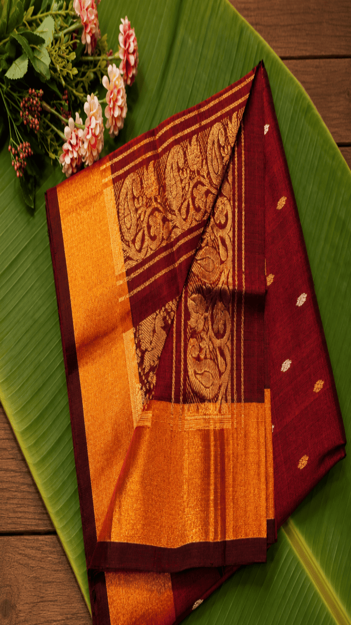 A maroon saree with gold border pallu design with silver and gold butta designs in the body 